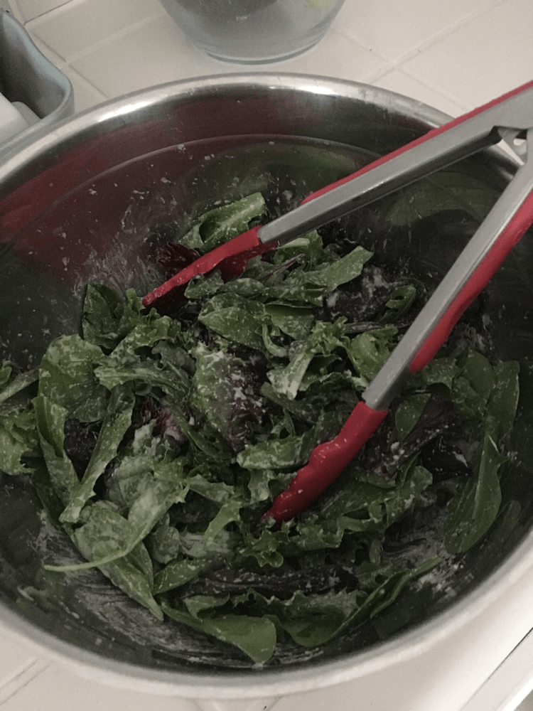 A bowl of nutrient-rich greens tossed with a pair of tongs, prepared by a certified nutritionist who emphasizes the importance of real food.