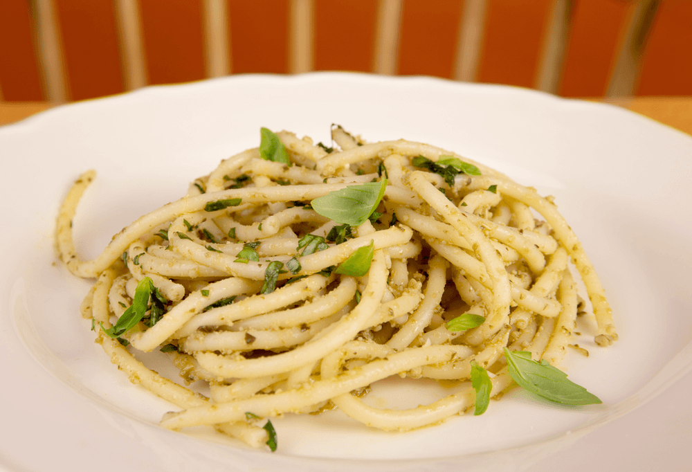A plate of spaghetti with fresh basil leaves on it.