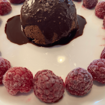 A decadent dessert with rich chocolate and luscious raspberries elegantly presented on a pristine white plate.