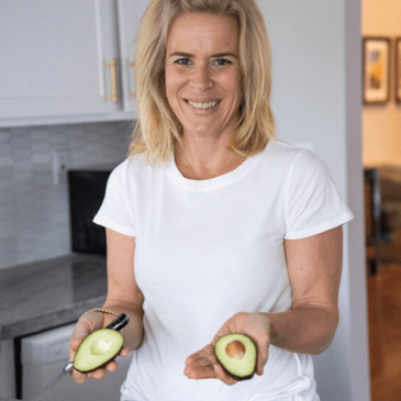 Nutritionist Molly Obert holding two avocados in her hands after slicing them open on a cutting board.