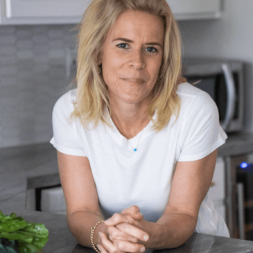 A Certified Nutrition Consultant Molly Obert in a white shirt leaning on a kitchen counter.