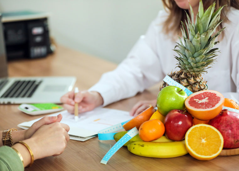 A Certified Nutrition Consultant is sitting at a desk with a basket of Real Food fruit.