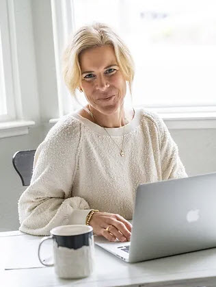 A Certified Nutrition Consultant passionately working at her desk, equipped with a laptop, delivering invaluable expertise in Real Food nutrition.